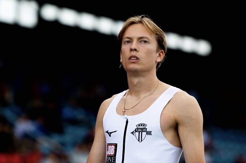 En friidrettsutøver i hvit Tjalve-singlet på et friidrettsstadion.