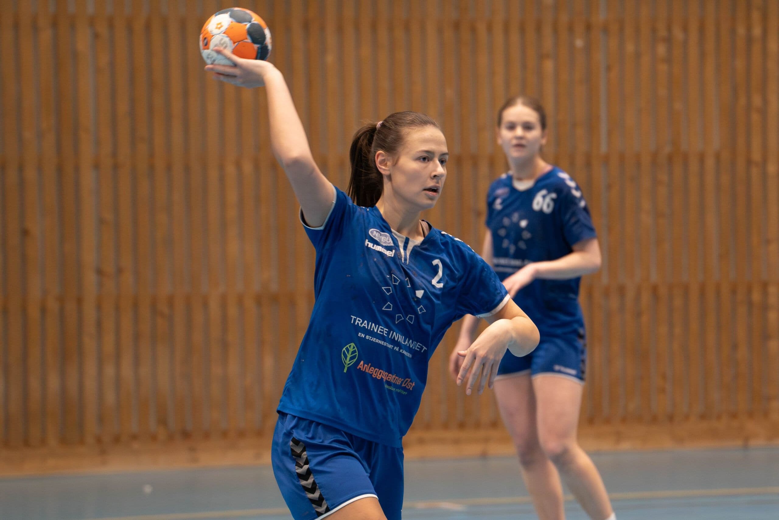 En håndballspiller i blå drakt gjør seg klar til å kaste ballen i en idrettshall.