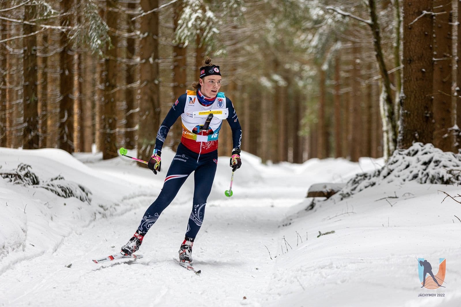 En langrennsløper i landslagsdrakt går i løypa i en snødekt skog under en konkurranse.