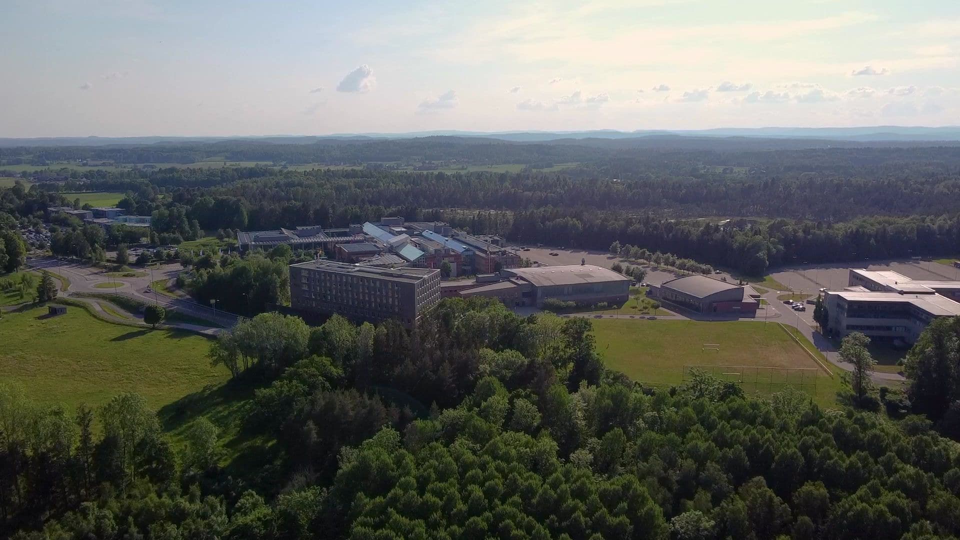 Flyfoto over et campusområde med bygninger omgitt av skog og åpne grøntområder.
