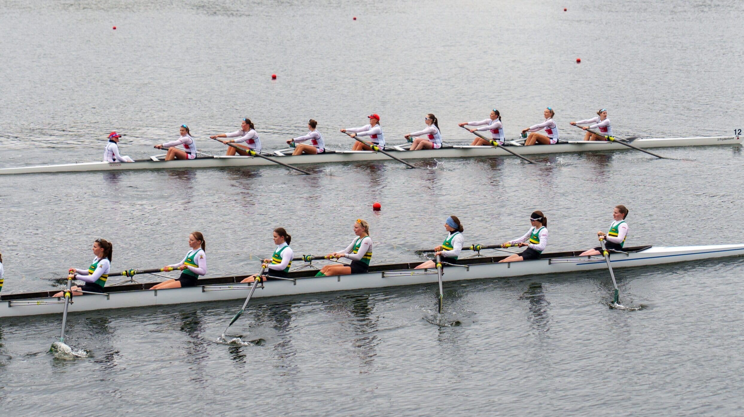 To robåter med åttere ror side om side i et regatta på vannet.