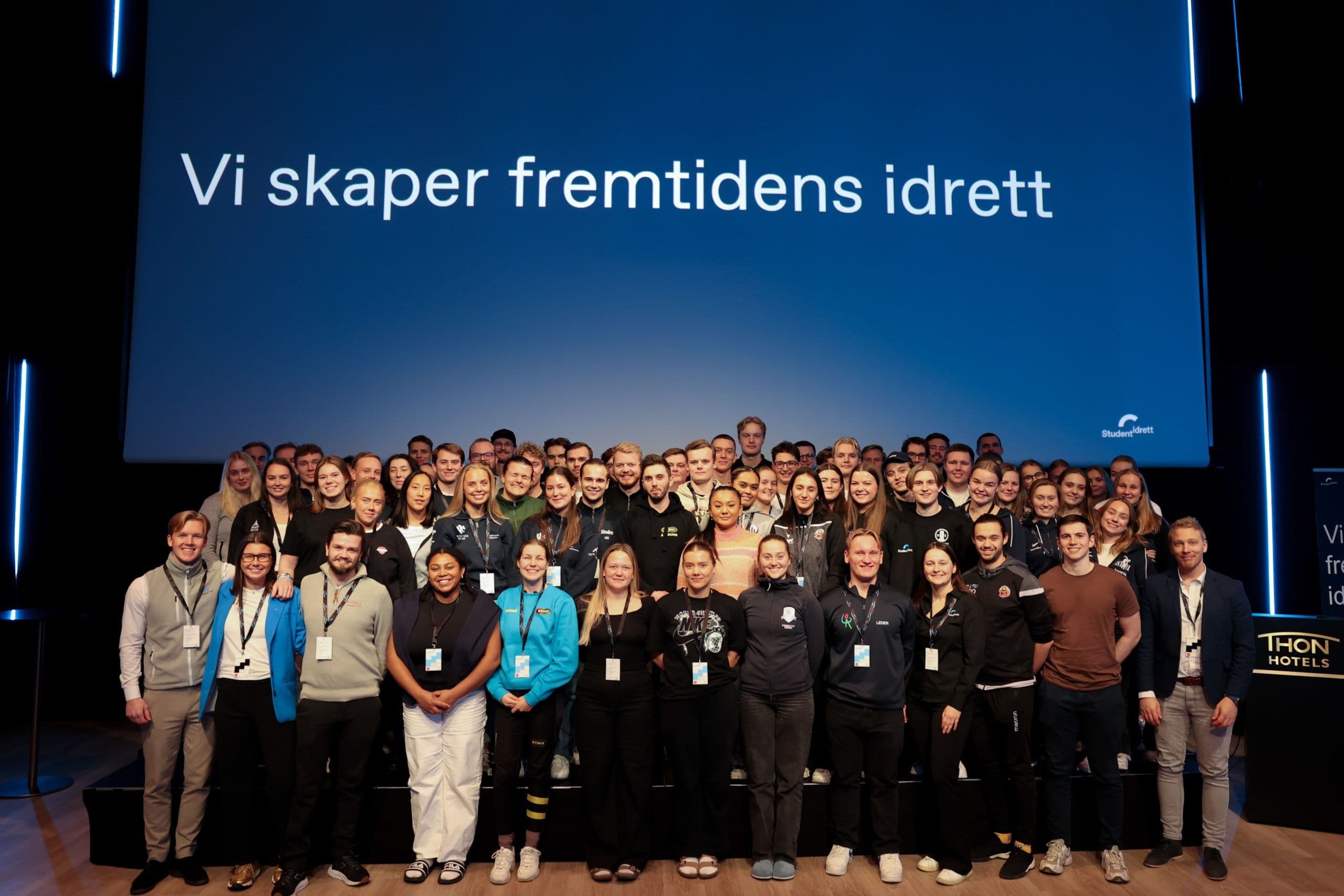 Stort gruppebilde av deltakere samlet i en sal foran storskjermteksten «Vi skaper fremtidens idrett».