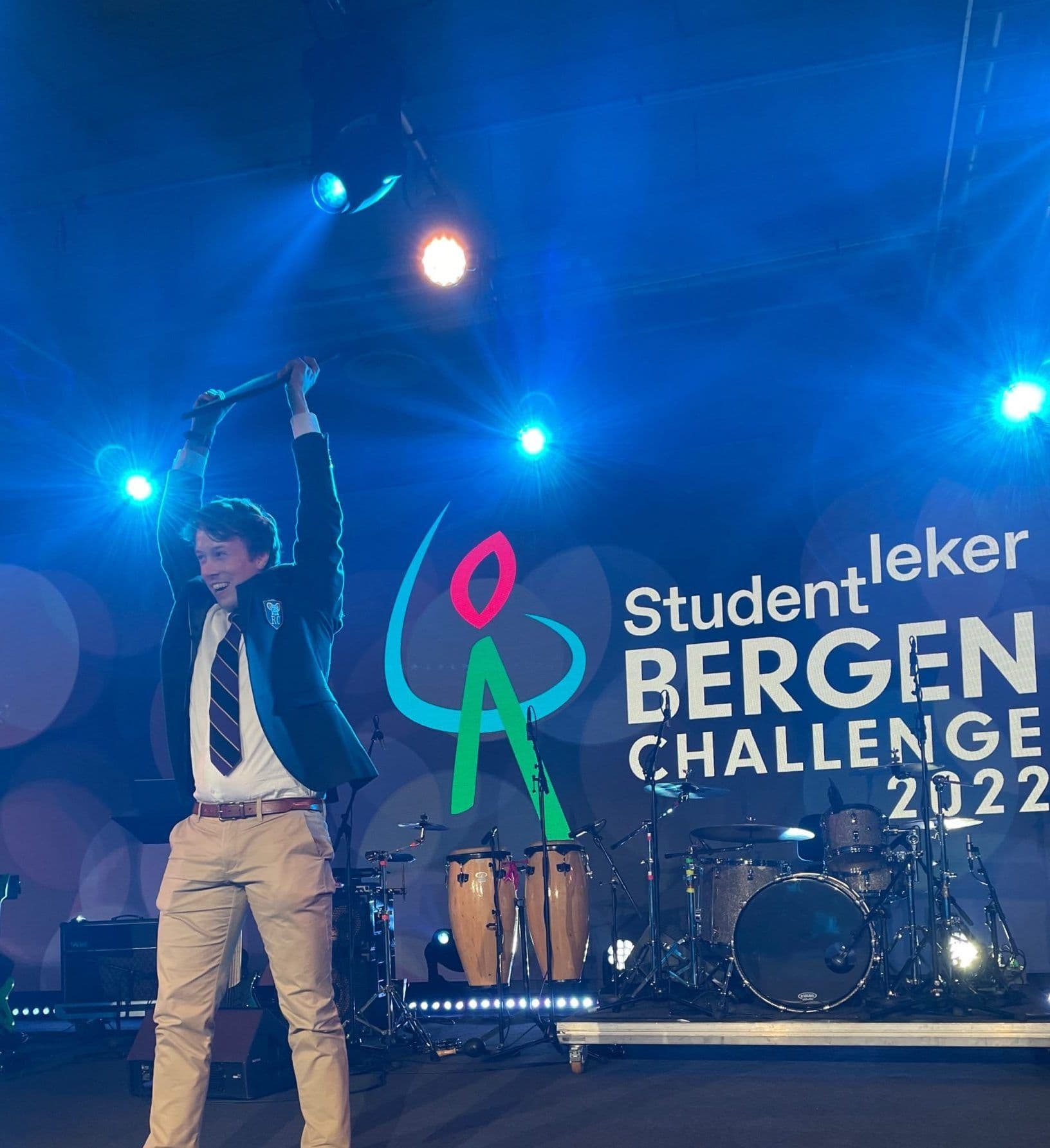 En mann jubler med hevet arm på en scene foran en skjerm med teksten Studentleker Bergen Challenge 2022.