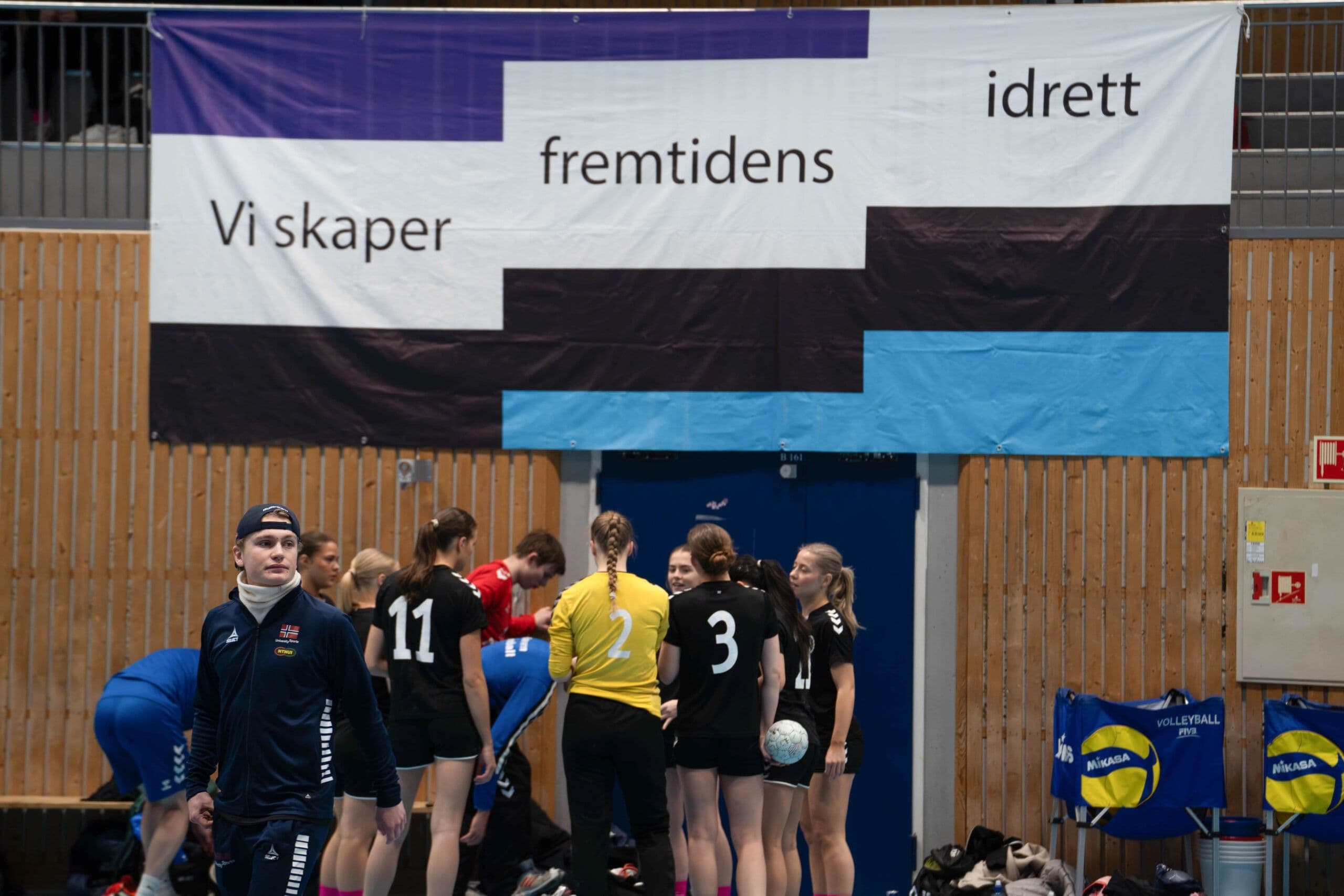 Et volleyballag samlet i en hall under et banner med teksten «Vi skaper fremtidens idrett».