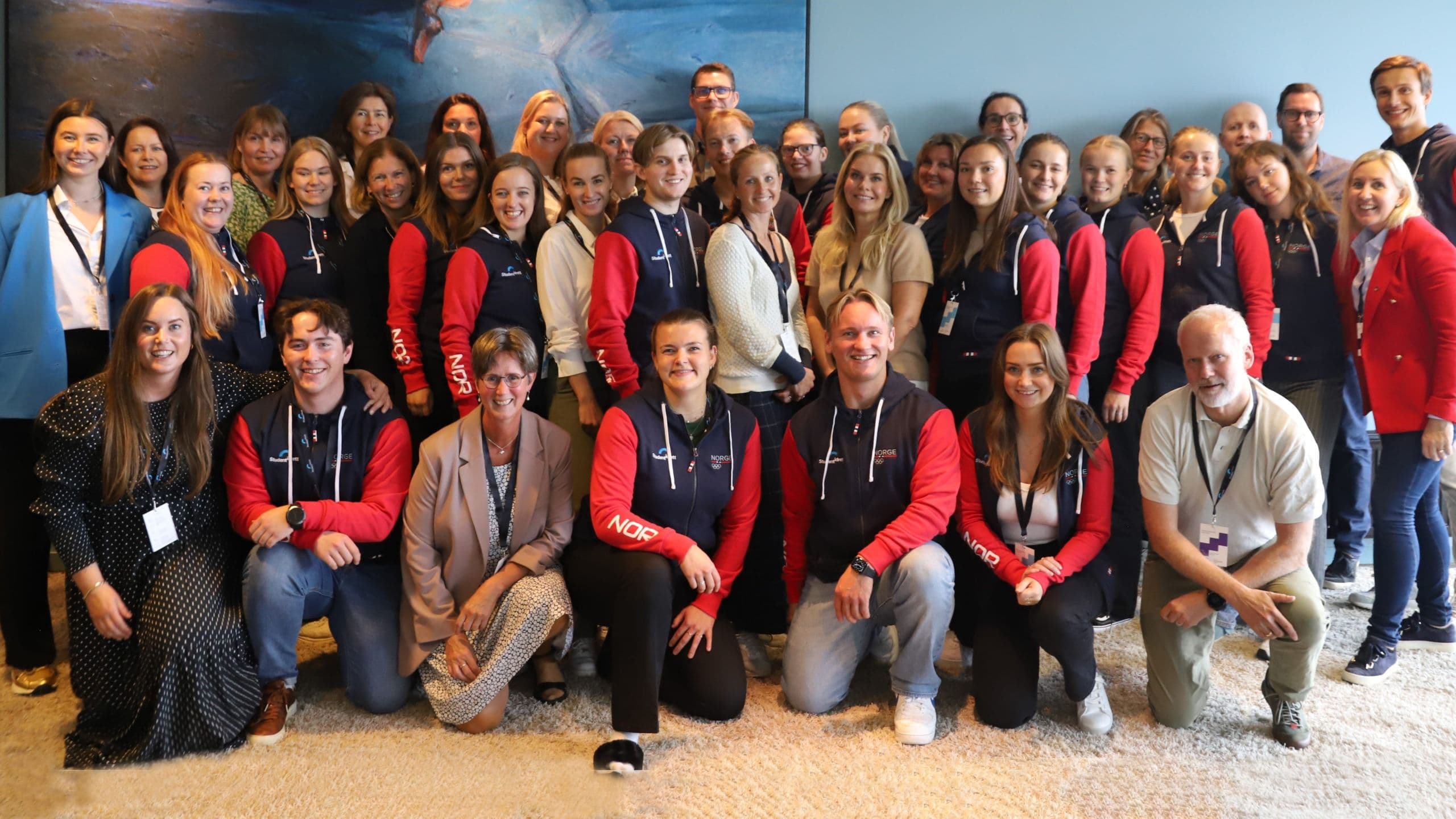 En stor gruppe studenter i røde og mørkeblå Norge-jakker samlet til et gruppebilde.