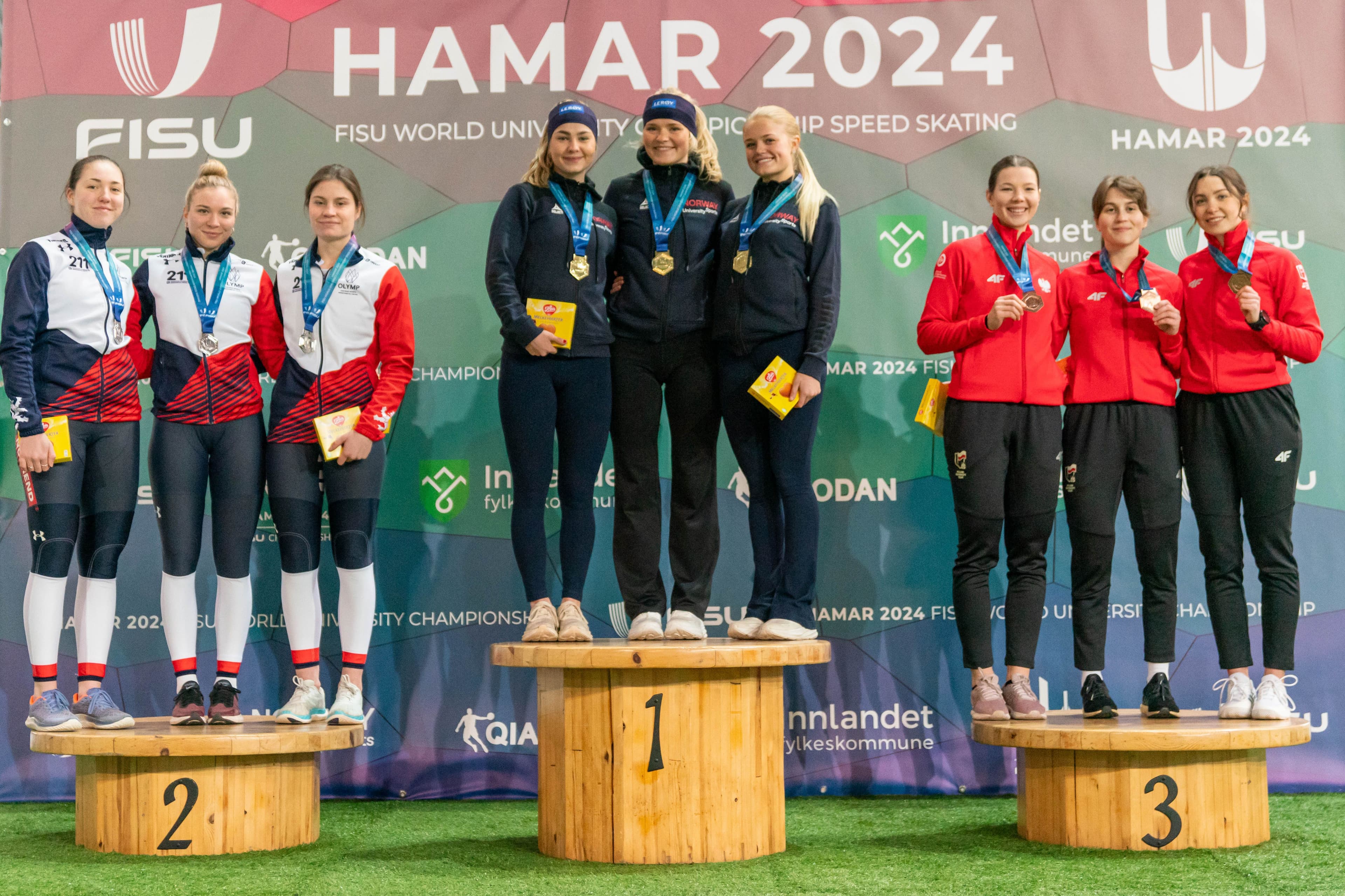 Tre kvinnelige skøyteløpere med medaljer på seierspallen foran en vegg med teksten Hamar 2024.