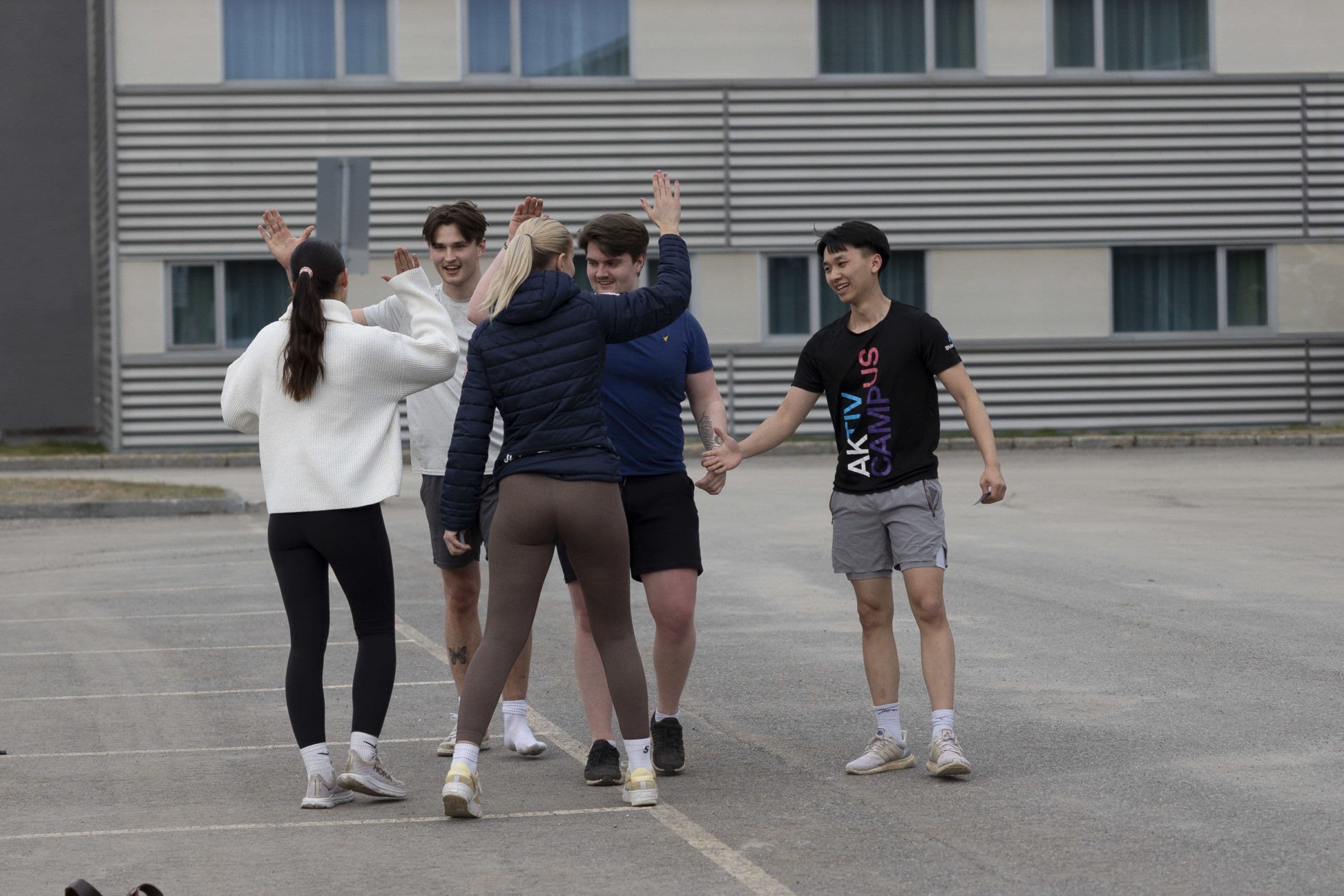En gruppe studenter gir hverandre high five på en asfaltplass foran en skolebygning.
