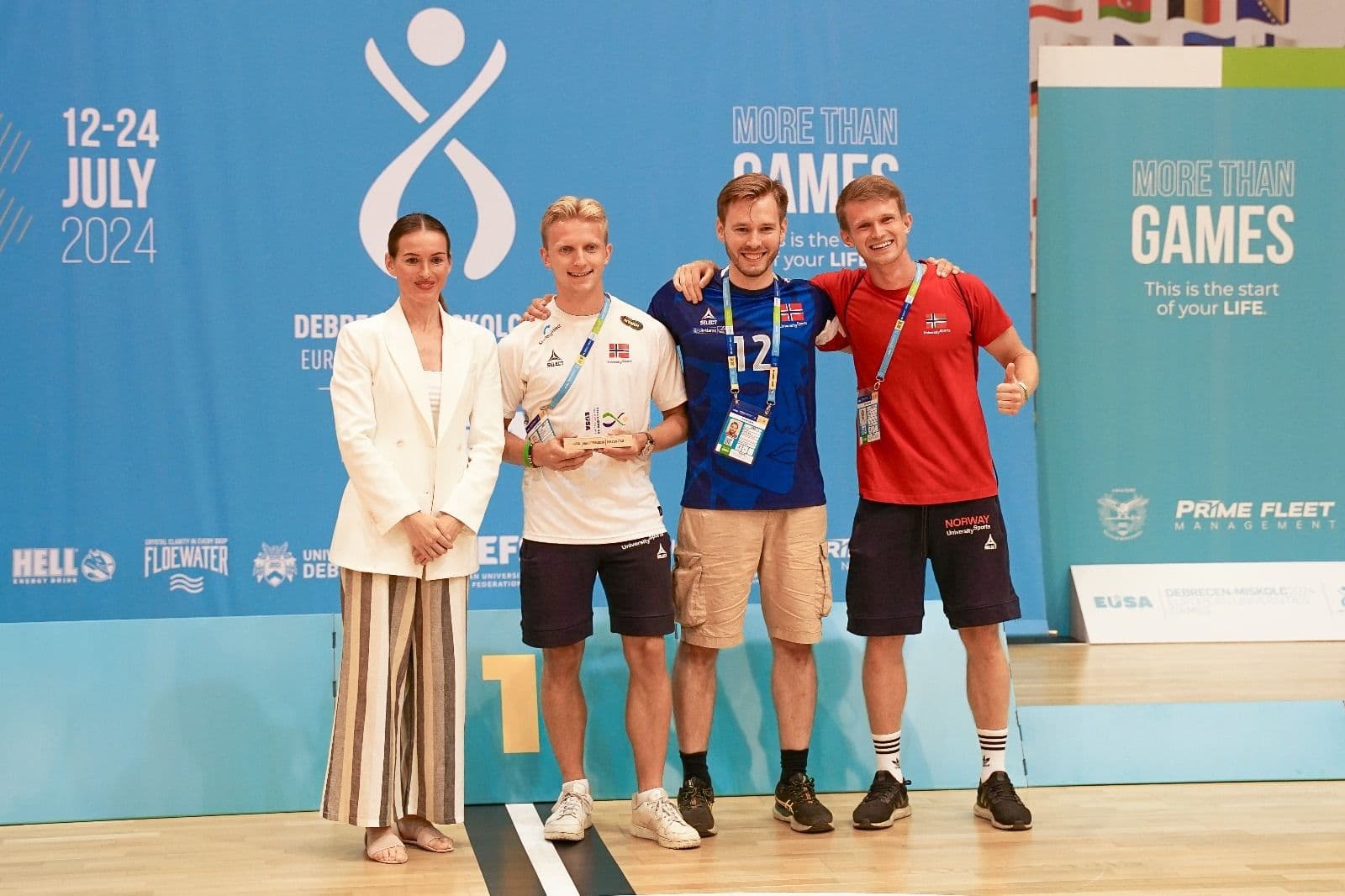 Fire personer poserer med en pokal foran en vegg fra Debrecen 2024 European Universities Games.