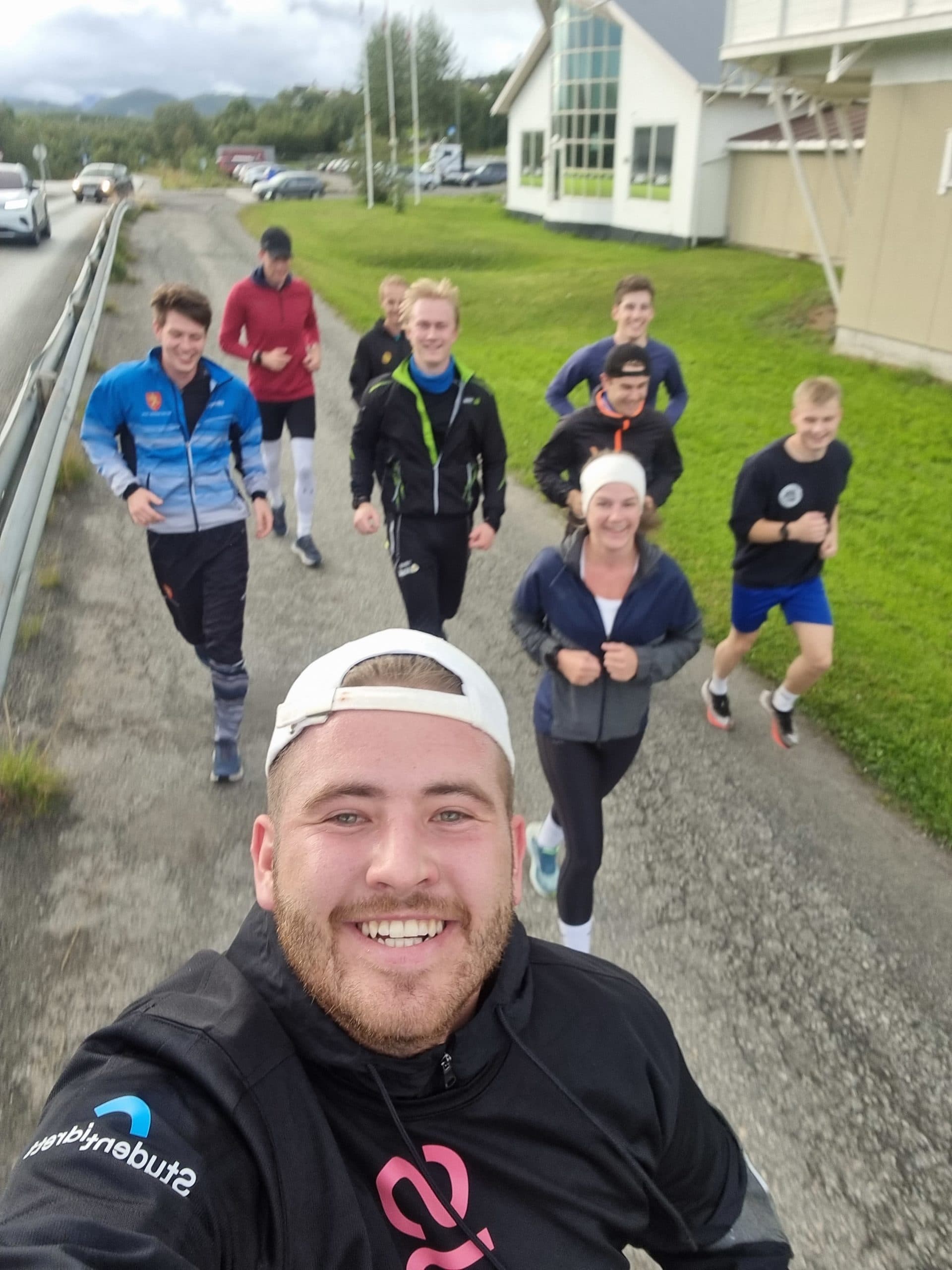 En gruppe studenter jogger langs en vei og tar en selfie mens de smiler mot kamera.