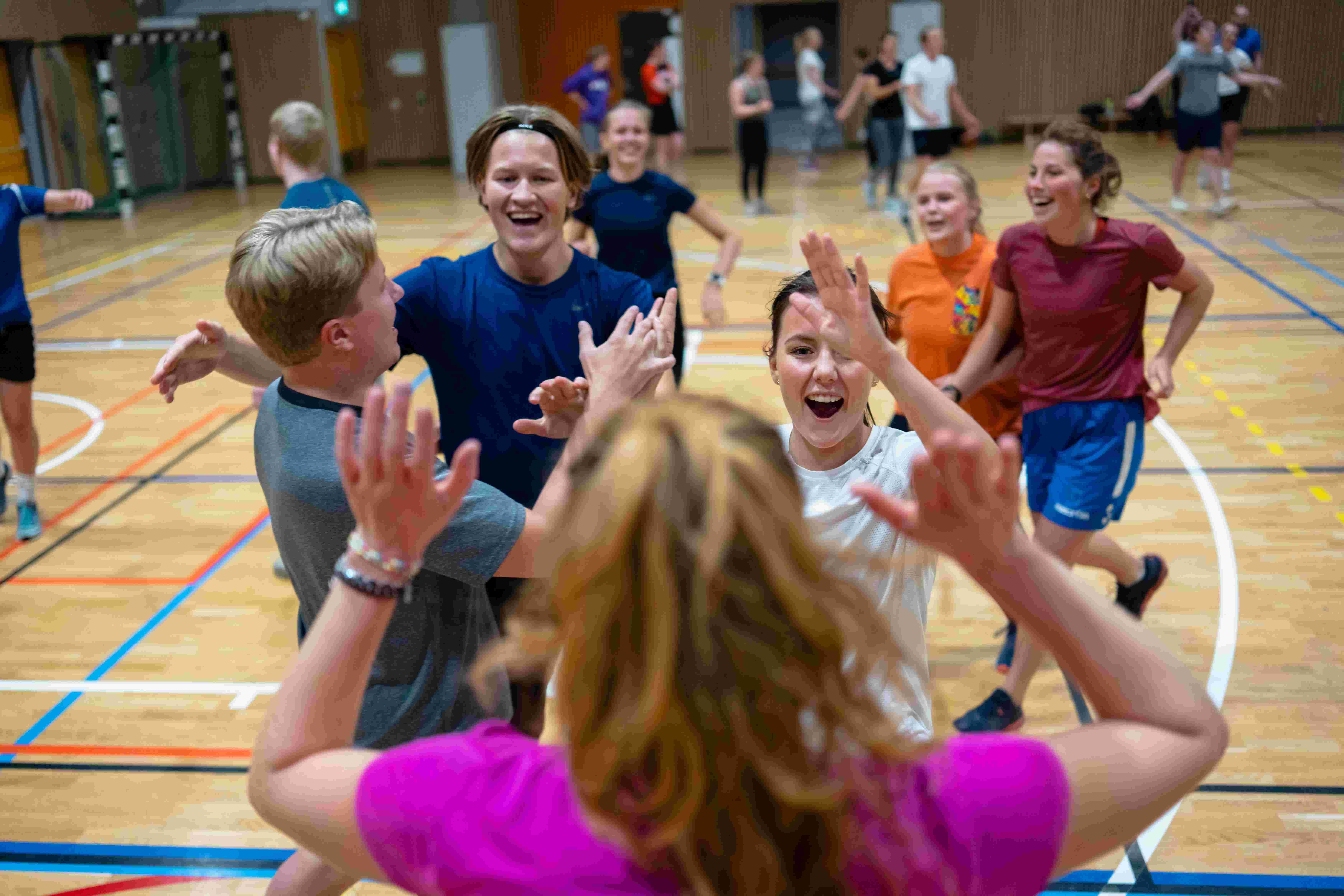 Smilende studenter gir hverandre high five under en aktivitet i en idrettshall.