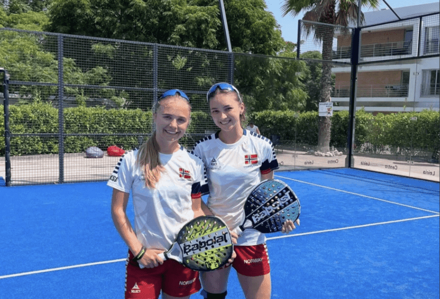To kvinner i norske landslagsdrakter holder padelracketer på en padelbane.