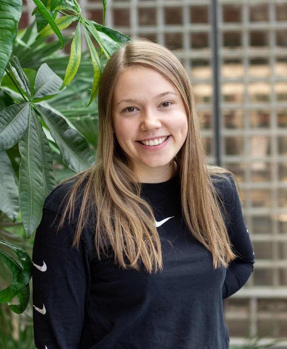 Portrett av en kvinne i svart genser foran en grønn plante.