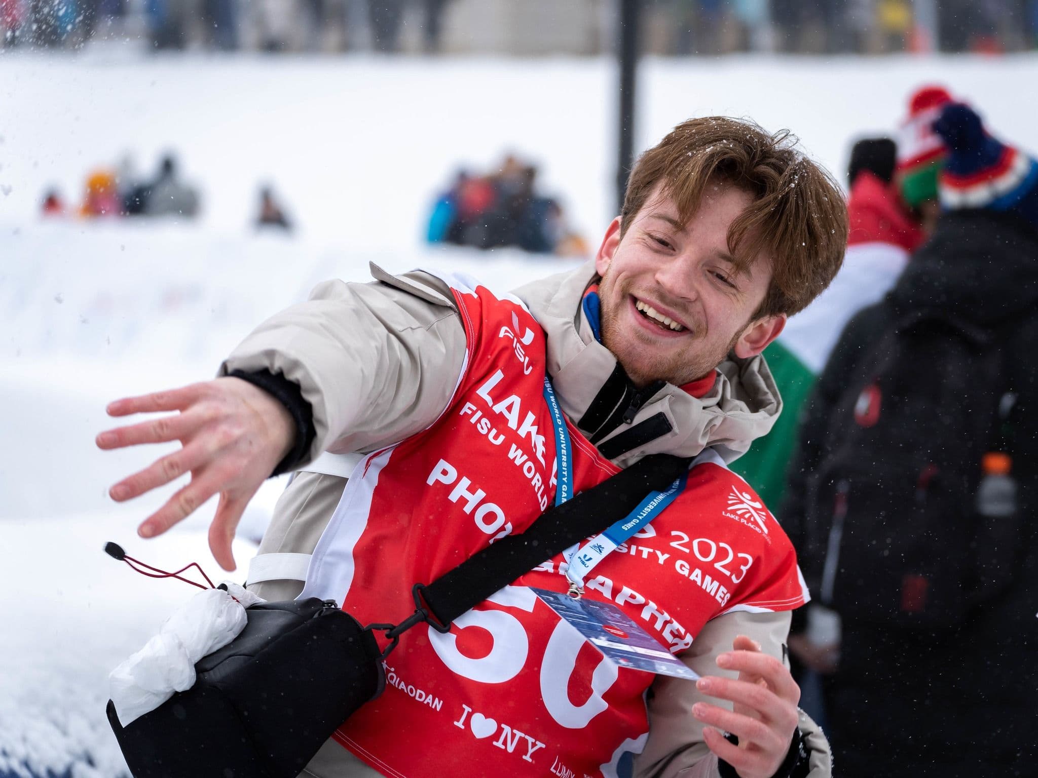 En smilende ung mann med startnummer kaster snø under FISU World University Games i Lake Placid 2023.