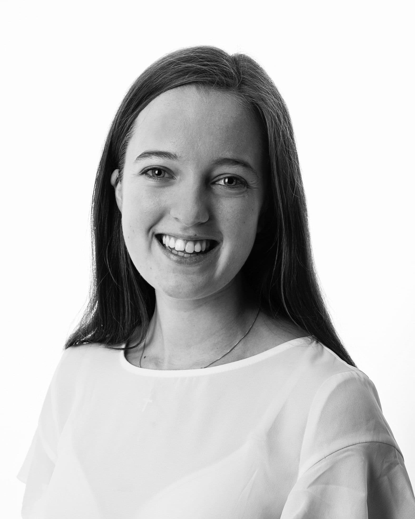 Portrett i svart-hvitt av en smilende kvinne i lys bluse mot hvit bakgrunn.