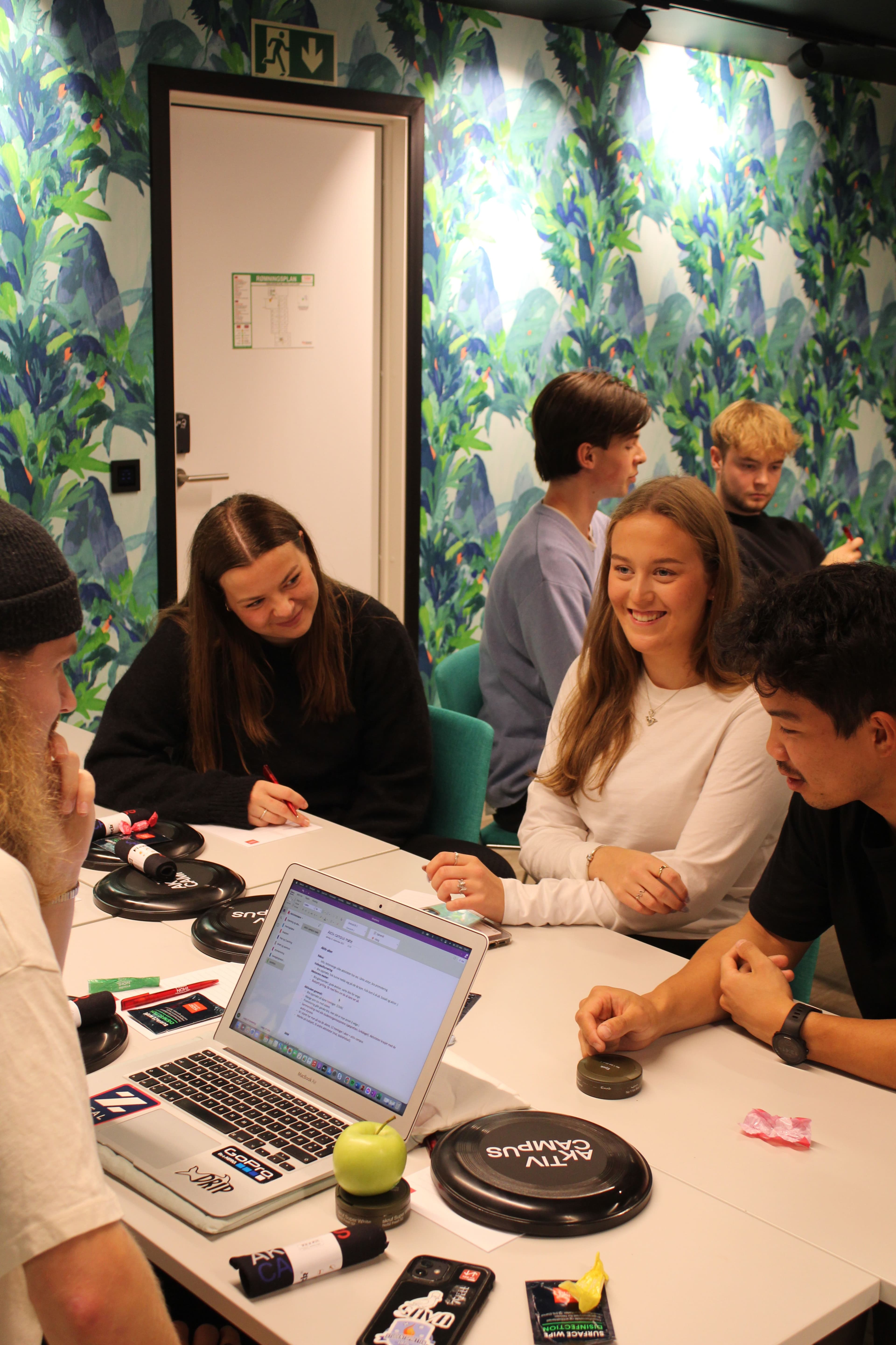 En gruppe studenter sitter rundt et bord med en laptop og spiller et spill.