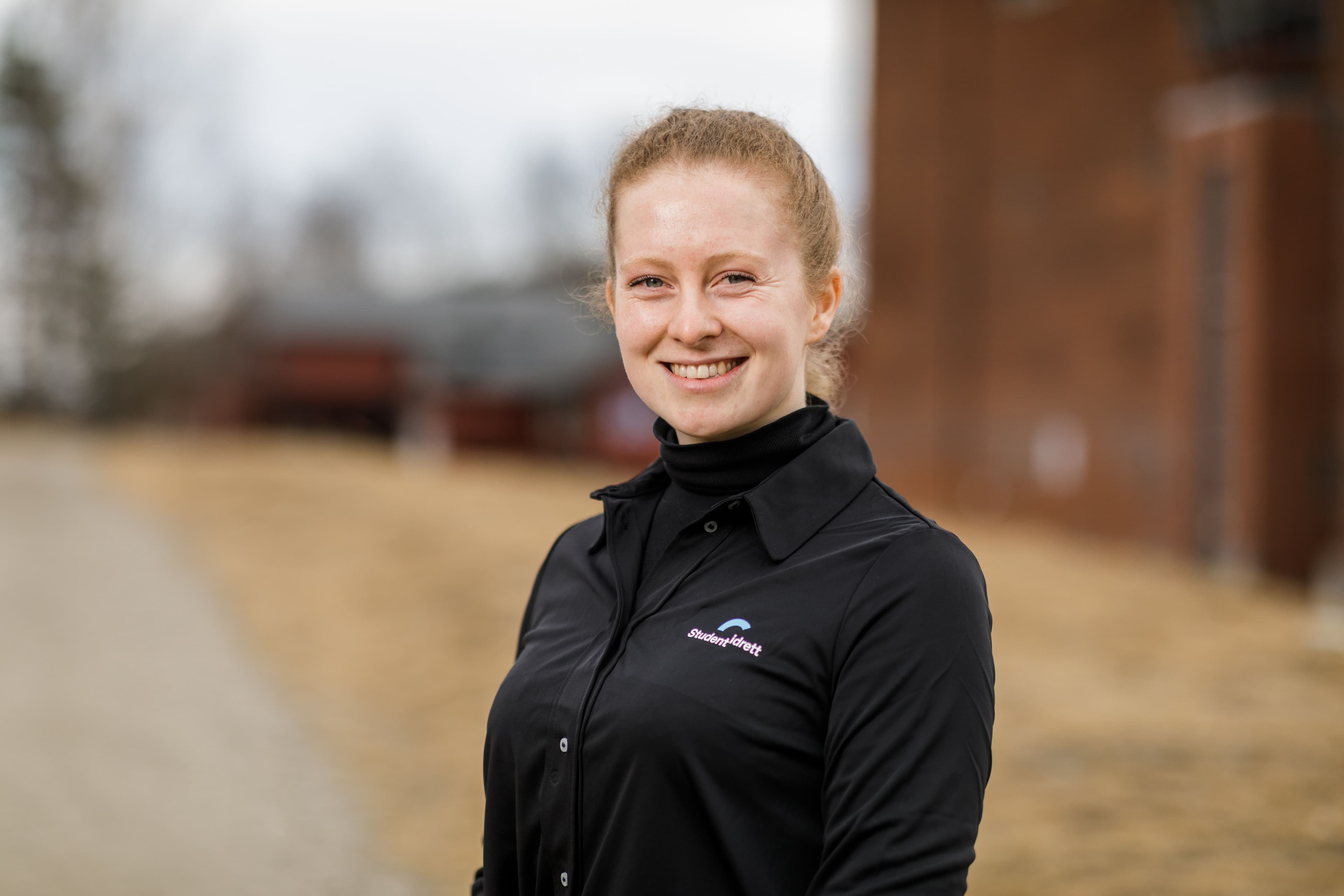 Portrett av en kvinne i svart Studentidrett-skjorte utendørs.