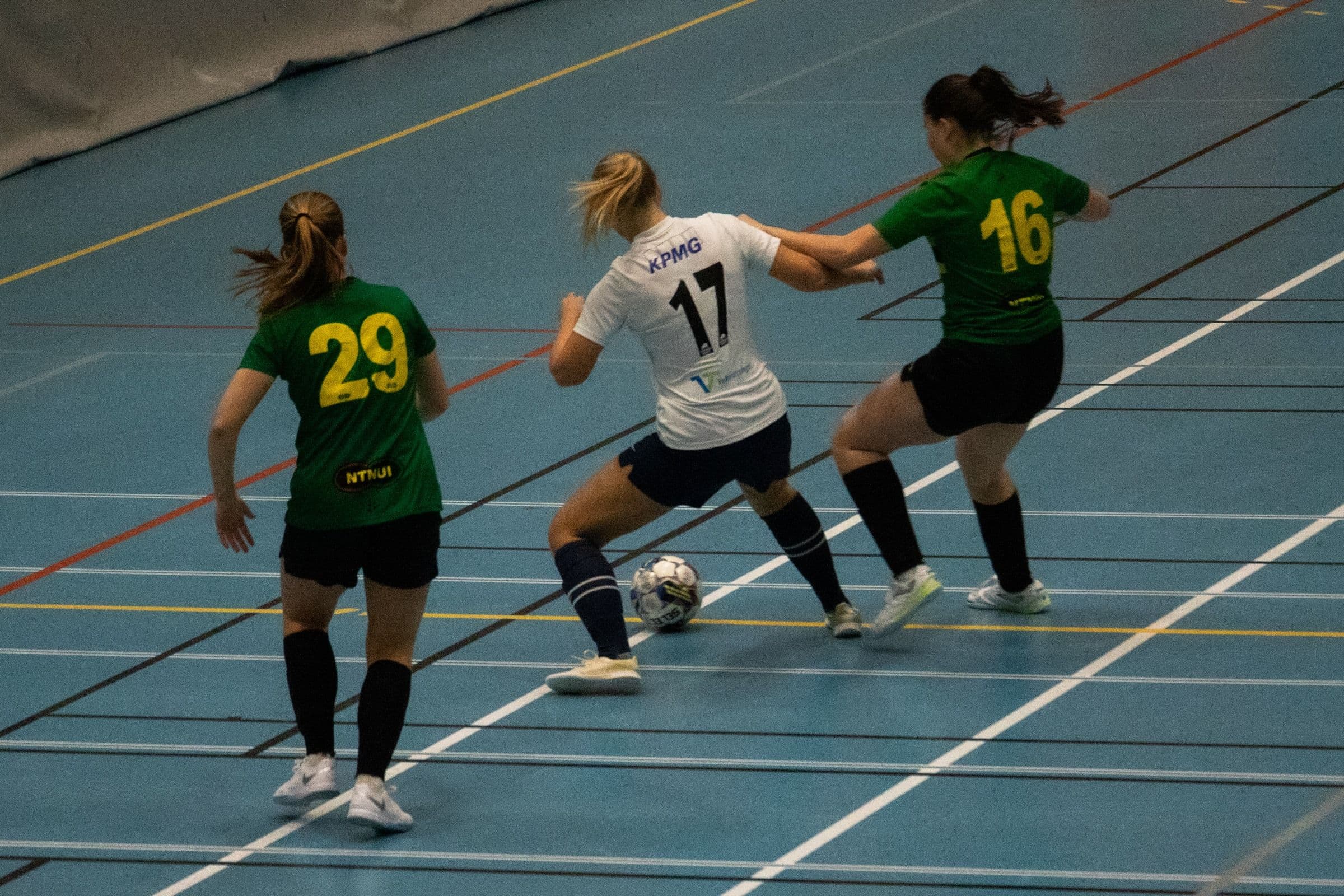 Kvinnelige futsalspillere kjemper om ballen i en idrettshall.