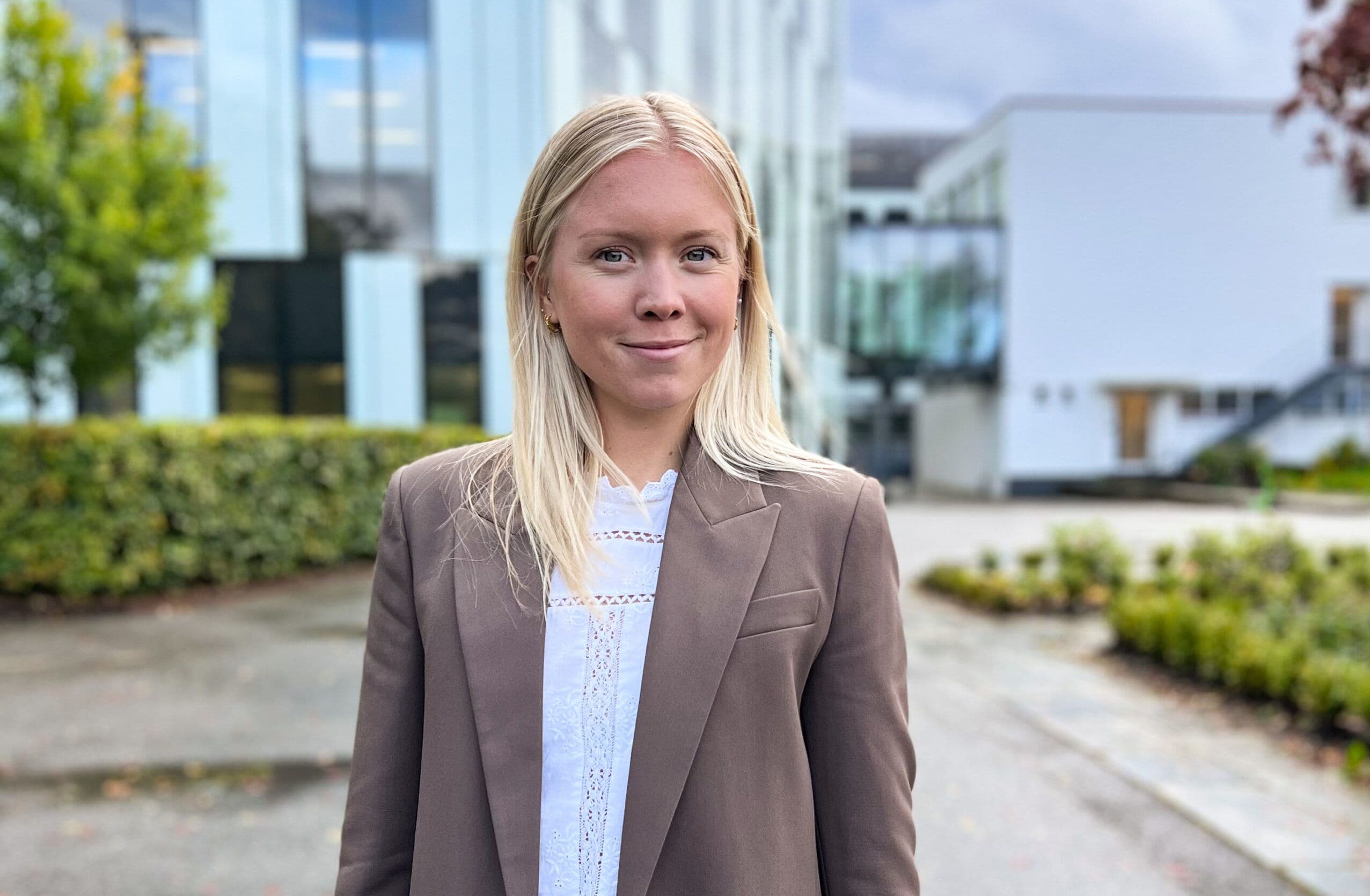 Portrett av en kvinne i brun blazer utendørs foran en bygning.