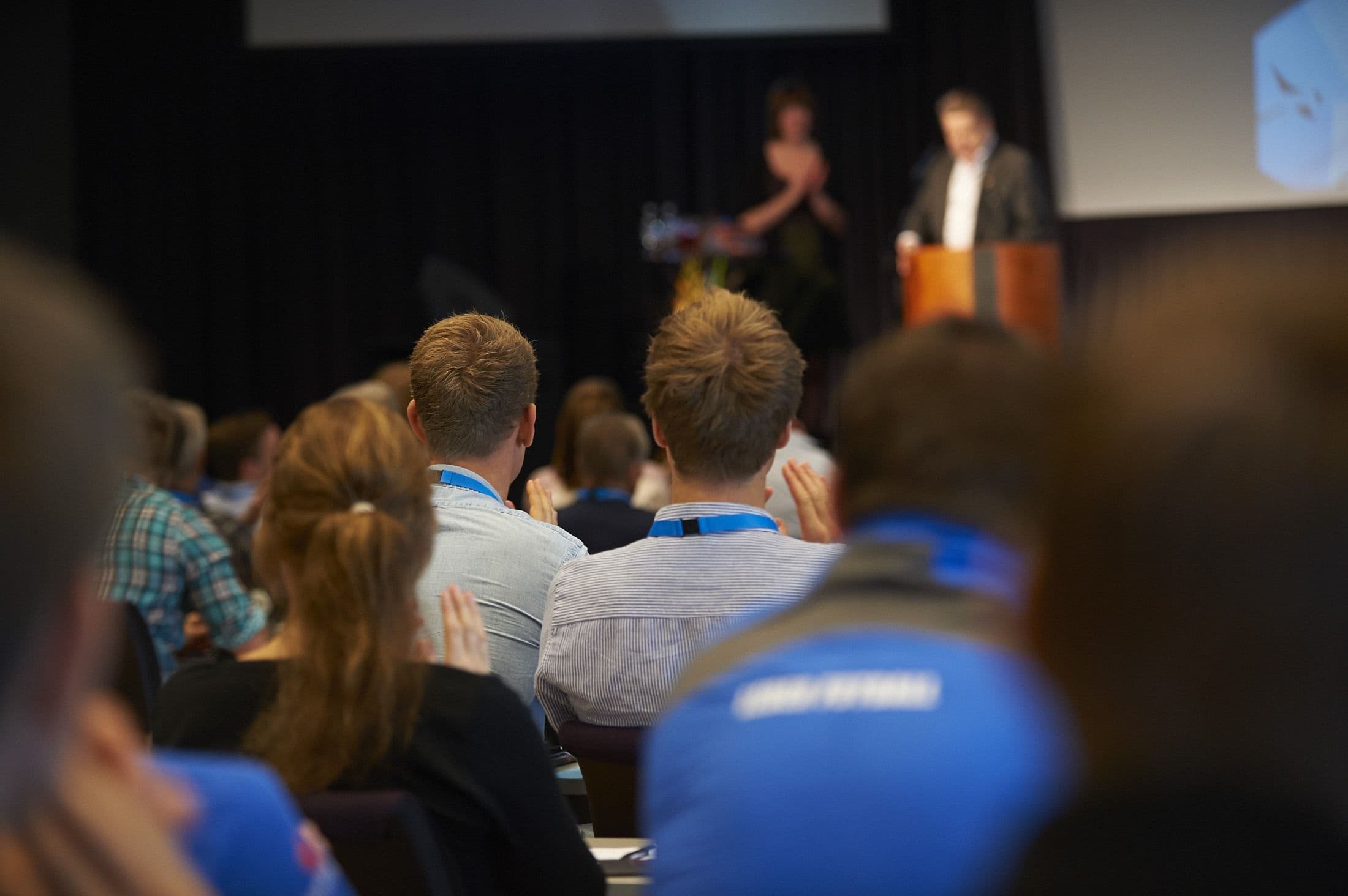 Et publikum av studenter som applauderer en person på en talerstol under et arrangement.
