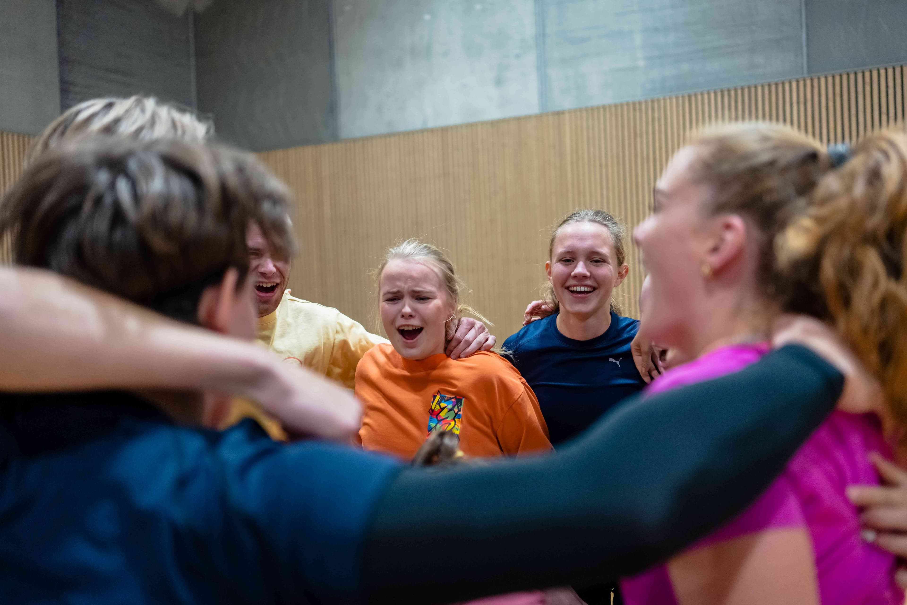 En gruppe jublende studenter som klemmer hverandre i en idrettshall.