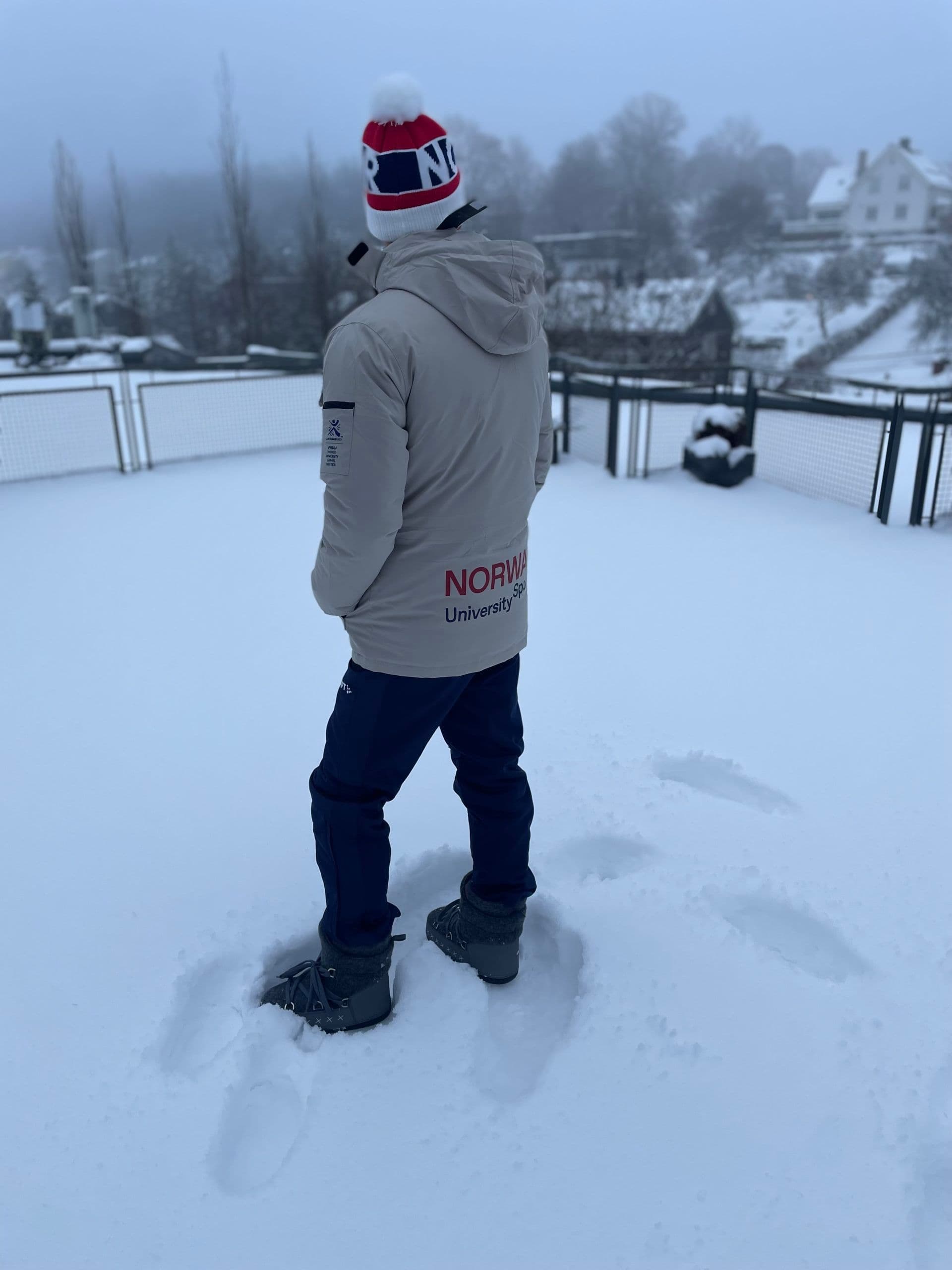 En person sett bakfra i jakke fra Norway University Sports står i dyp snø.