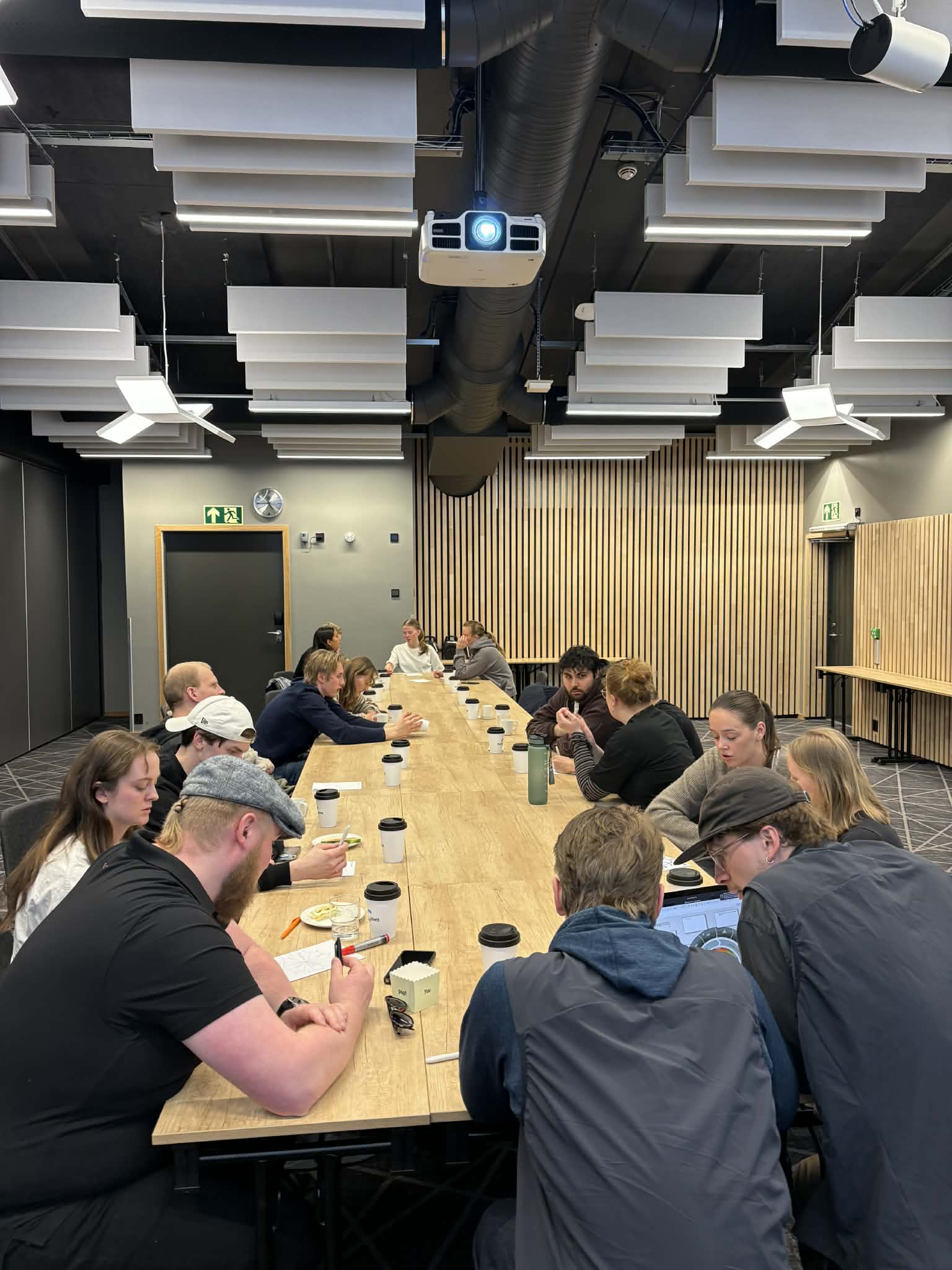 En gruppe mennesker sitter samlet rundt et langbord i et møtelokale.