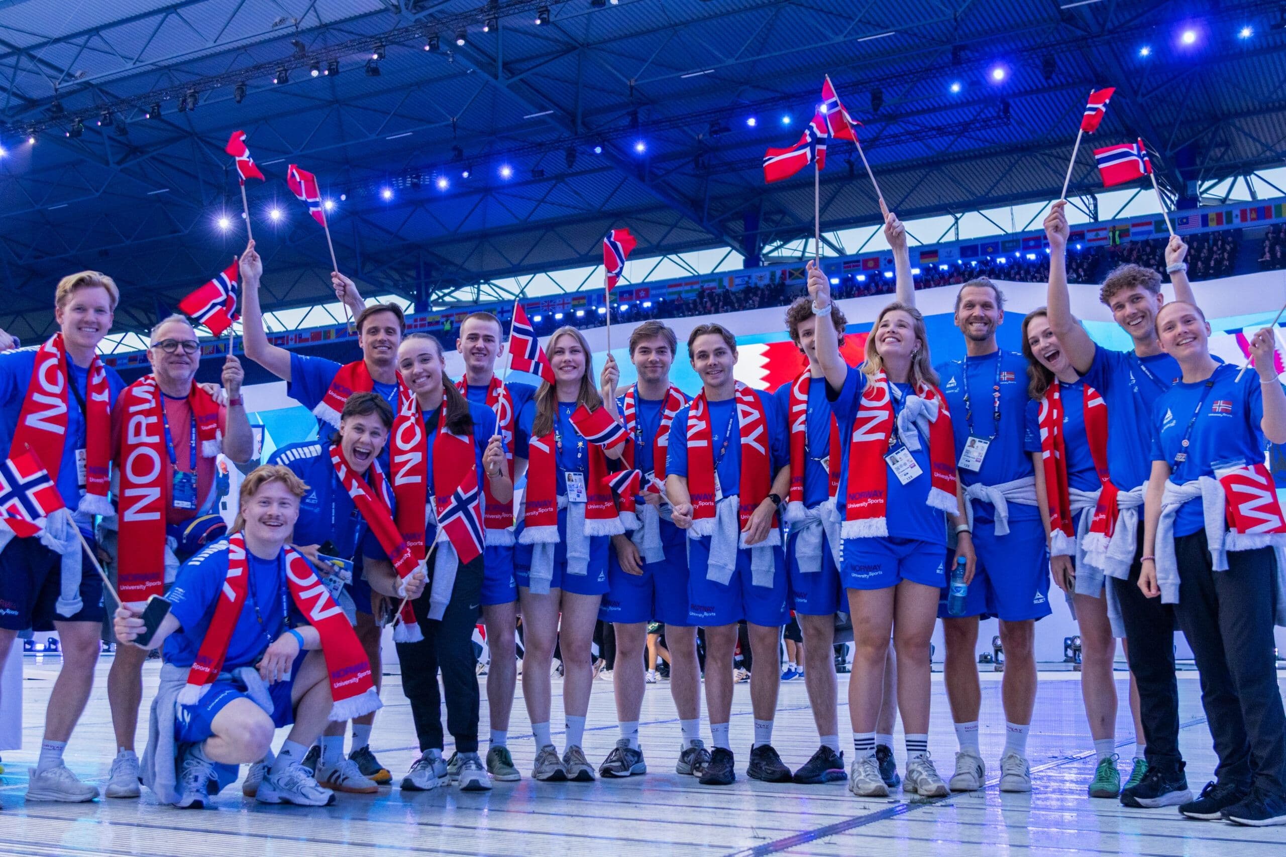 En gruppe norske studentutøvere med flagg og «Norway»-drakter i en idrettshall.