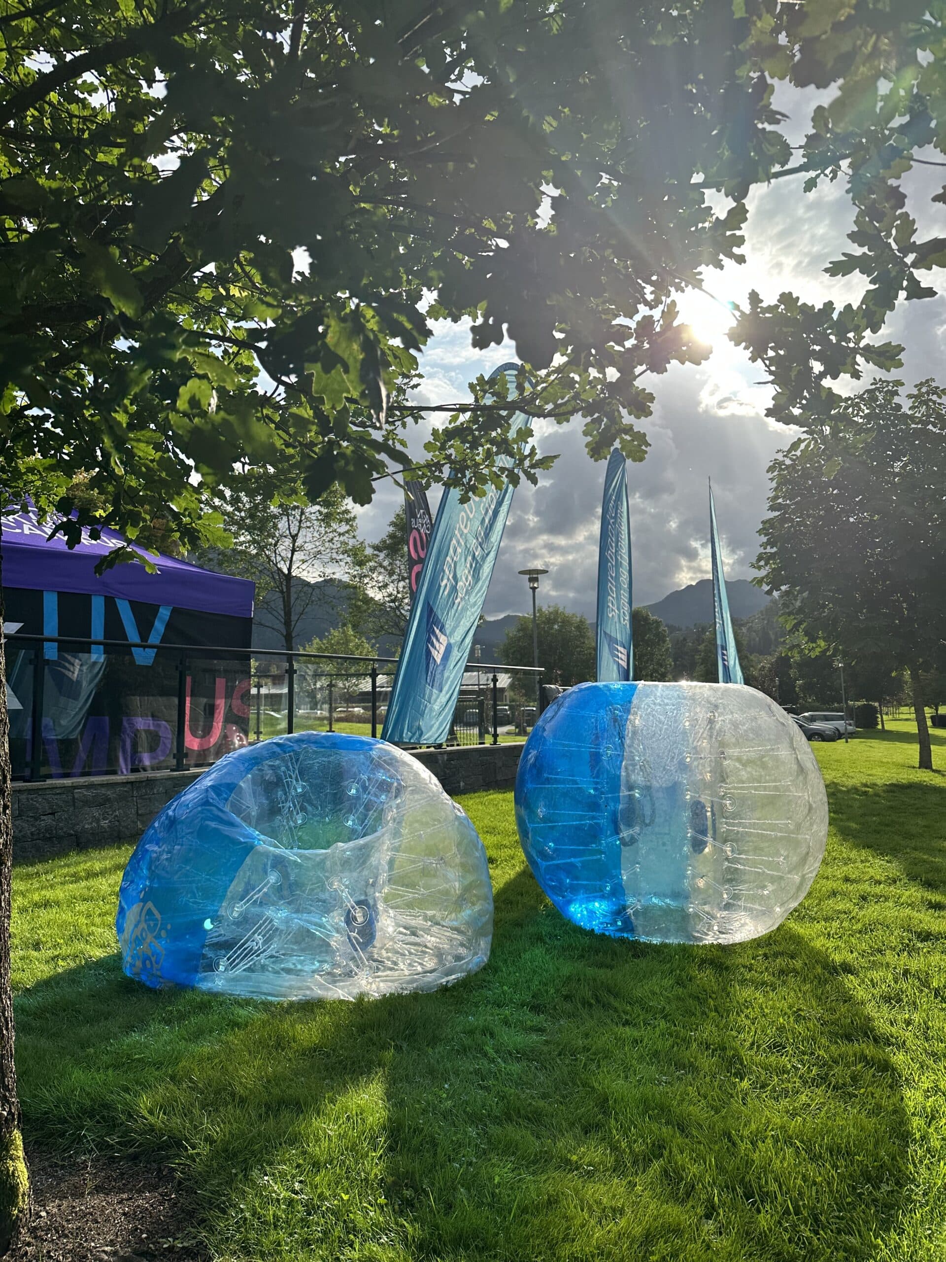 To bobleballer for bumperball ligger på gresset i en park i solskinn.