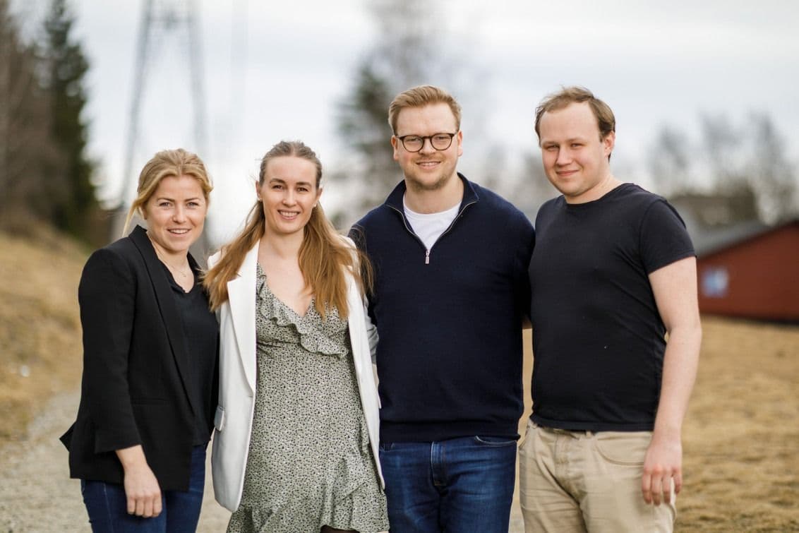Portrett av fire personer som står sammen utendørs i et landlig område.