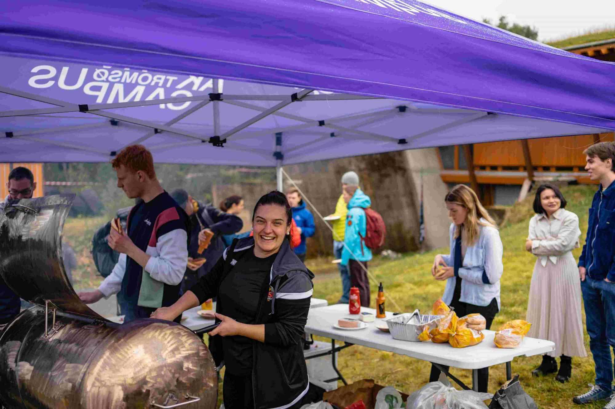 En smilende student griller mat under et Aktiv Campus-telt fra UiT Norges arktiske universitet.
