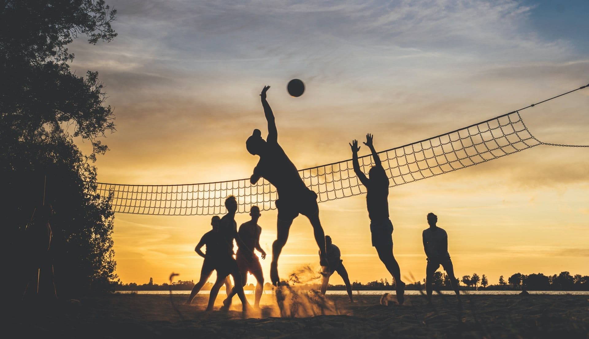 Silhuetter av personer som spiller sandvolleyball ved et nett i solnedgang.